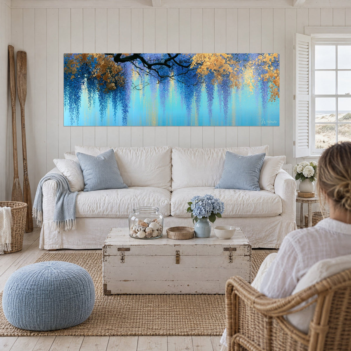 Schilderij blauwe regen in turquoise en gouden trossen onder een zwarte tak, crèmewitte muren, boven een bank in een lichte woonkamer