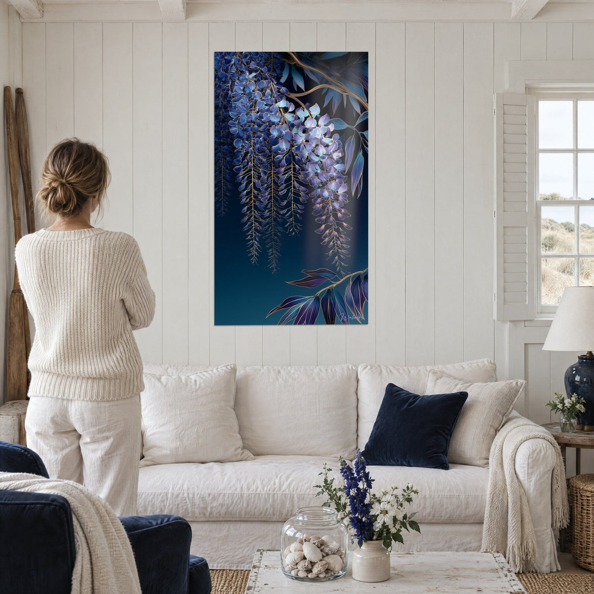 Cuadro de glicinias azul violeta en racimos colgantes con contornos dorados, mujer de espaldas, sobre un sofá en un salón luminoso