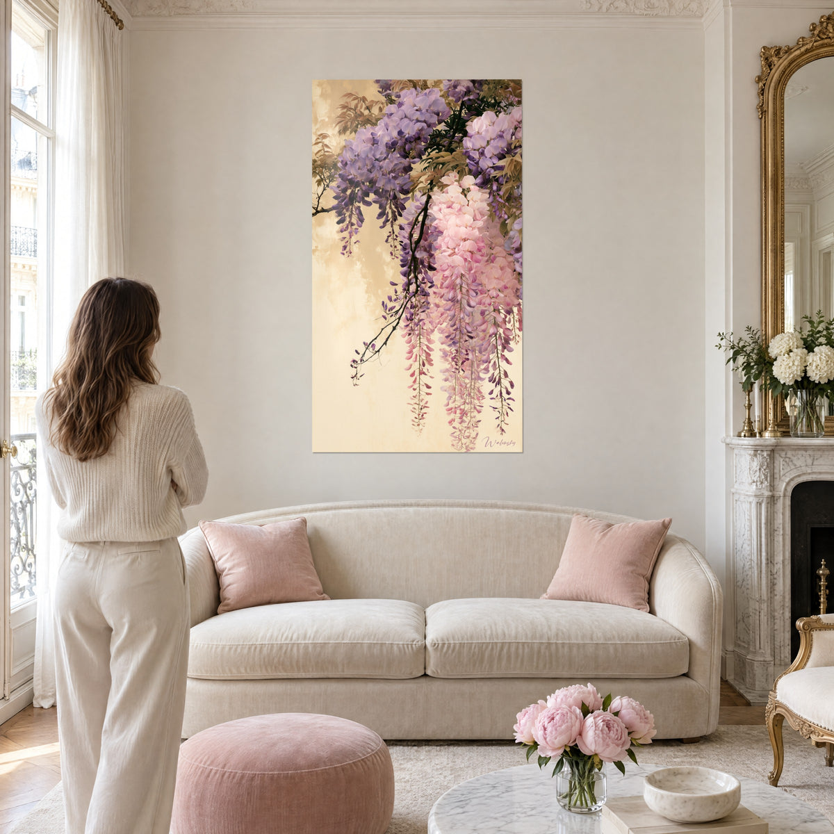 Quadro glicine a cascata di grappoli viola e rosa su fondo sabbia, donna di spalle, sopra un divano in un soggiorno luminoso