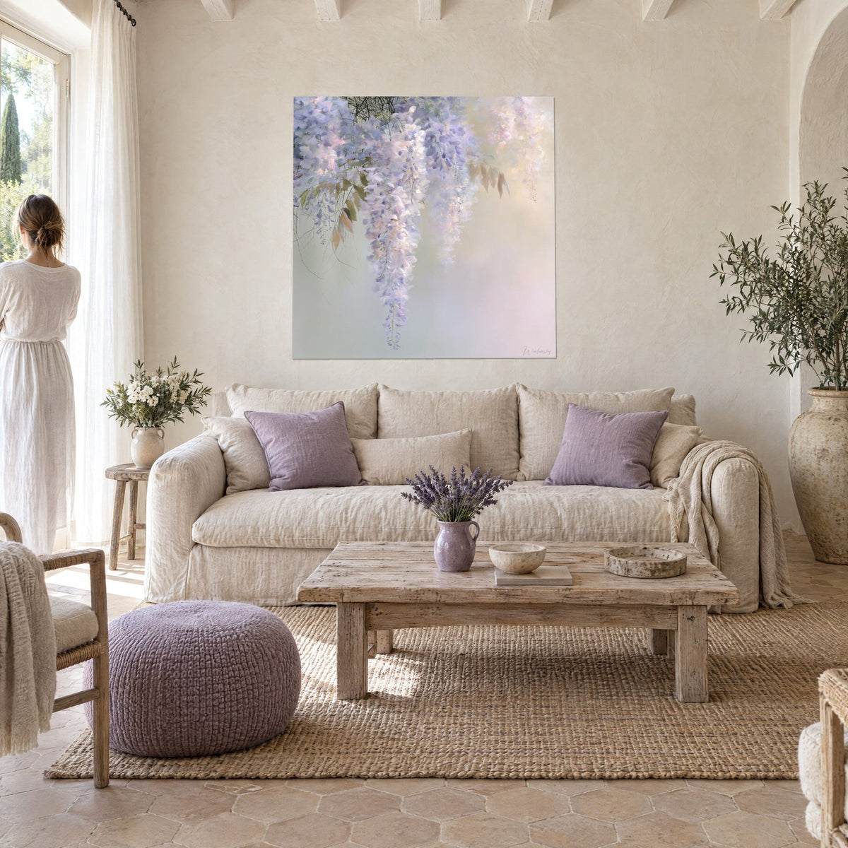 Quadro glicine in grappoli lilla e bianchi su foschia dorata, foglie ramate, due figure di spalle, sopra un divano in un soggiorno luminoso