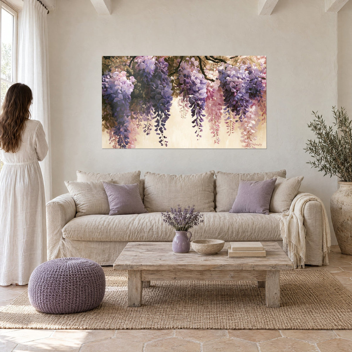 Quadro grappoli di glicine a cascata in lilla e rosa su fondo avorio, guardato da una donna di spalle, sopra un divano in un soggiorno luminoso