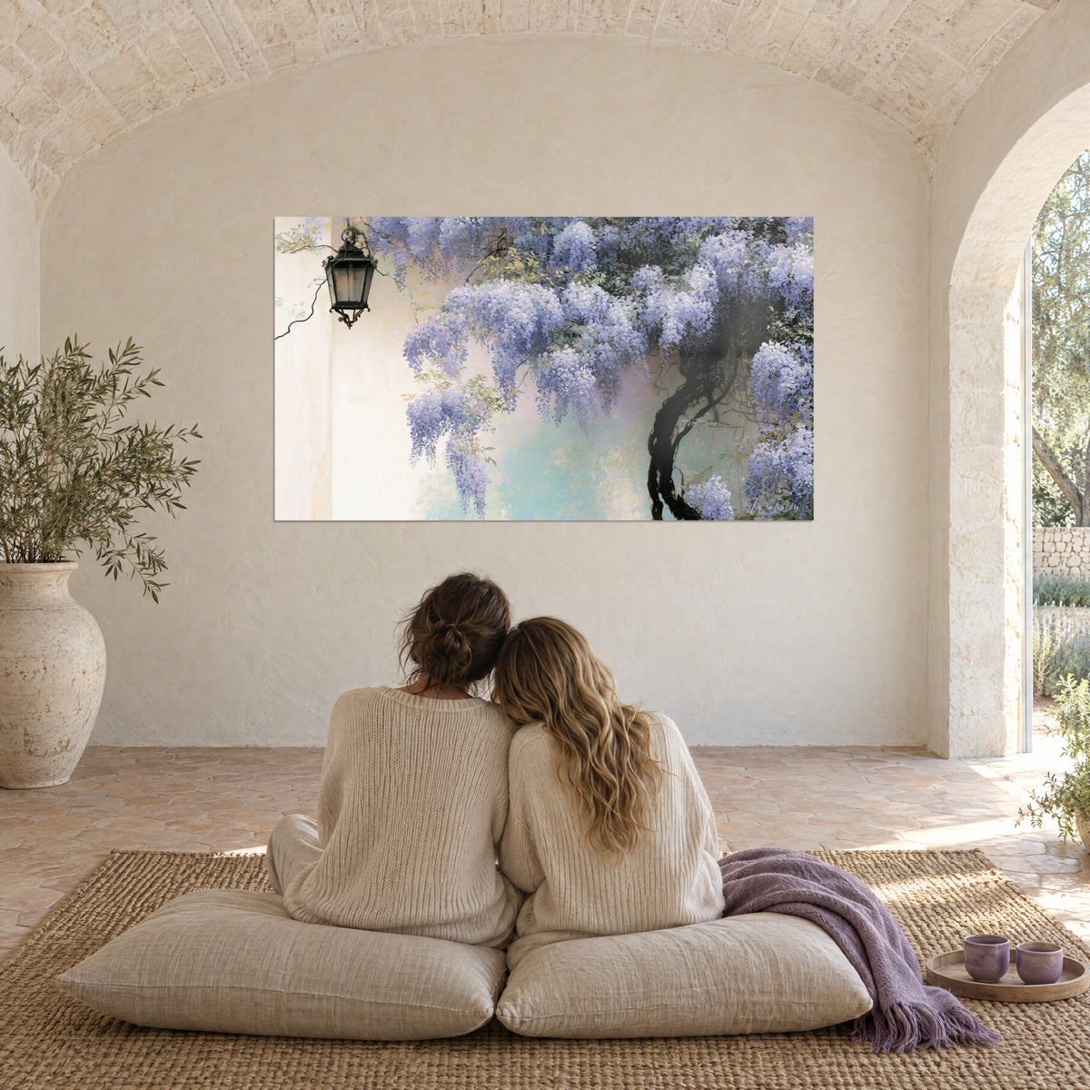 Wall art with violet wisteria and tender green foliage, black lantern, two young women seen from behind embracing on cushions