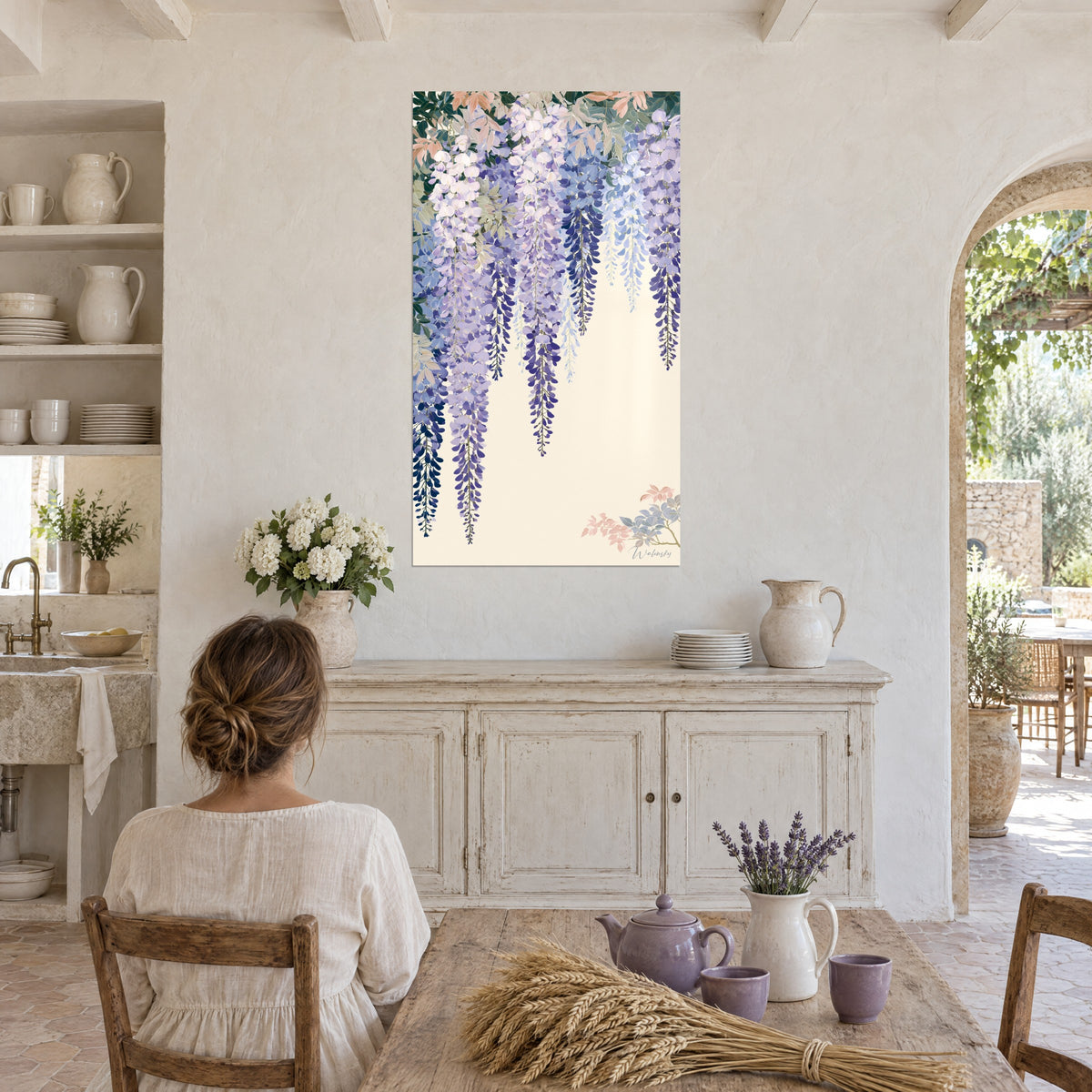 Schilderij gordijn van lavendelkleurige en nachtblauwe blauweregenbloemen, vrouw van achteren aan tafel naast een boeket, in een keuken van steen