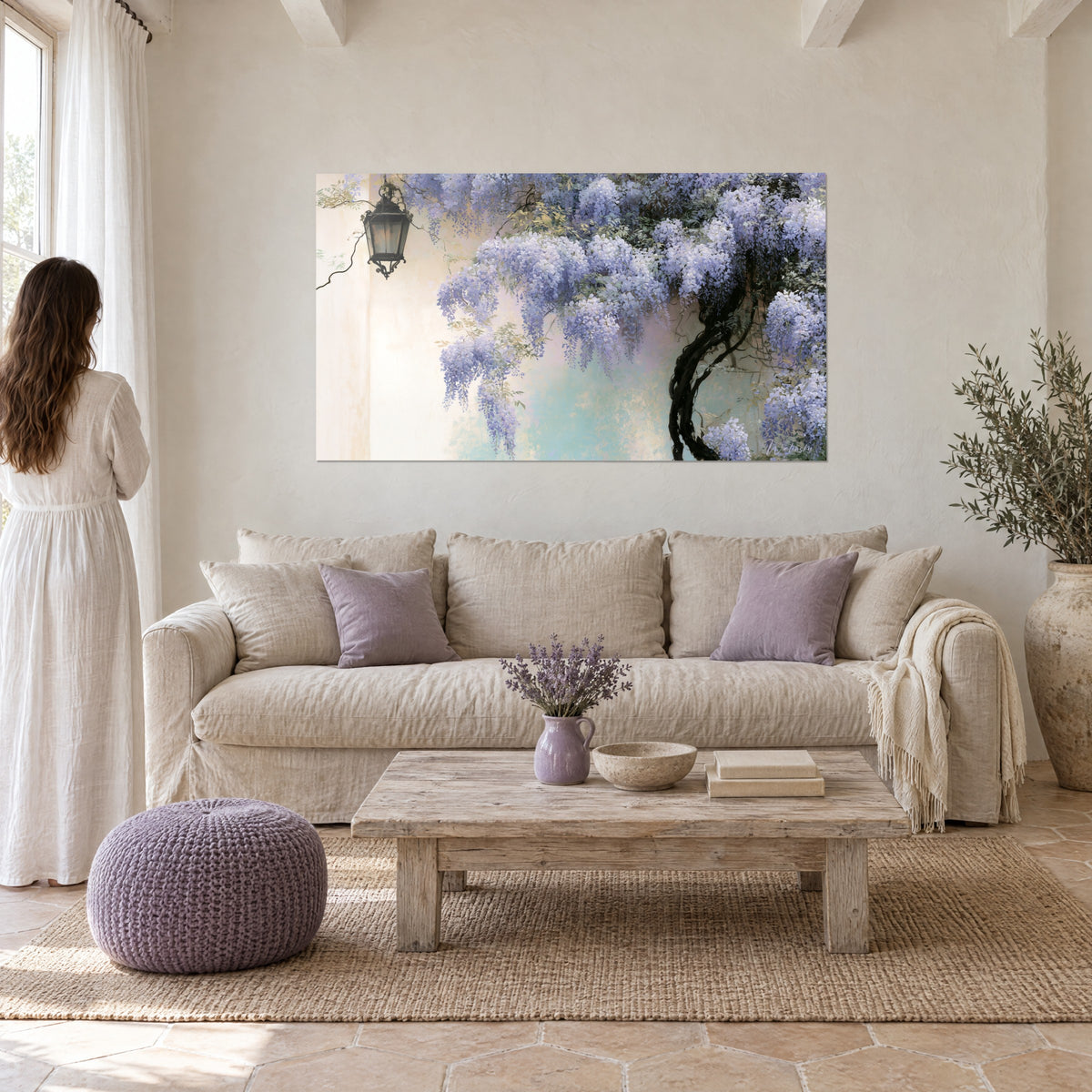 Wall art with cascading mauve wisteria clusters on a cream wall, black wrought-iron lantern, woman seen from behind above a sofa in a bright living room