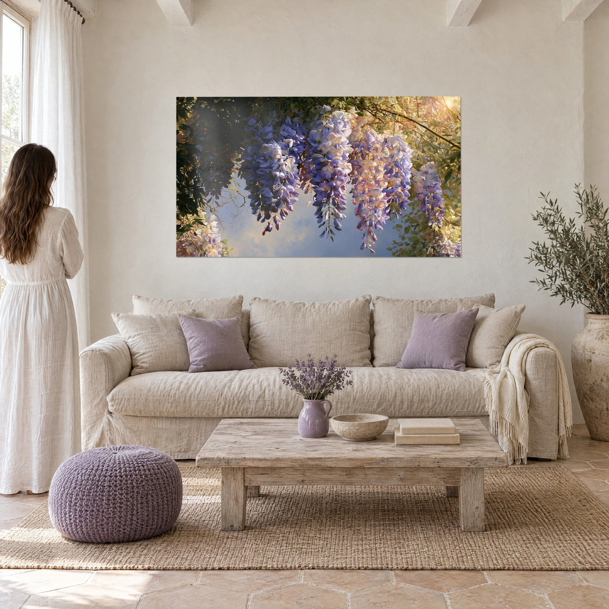 Quadro glicine in grappoli malva e rosati sotto controluce dorata, una donna di spalle, sopra un divano in un soggiorno luminoso