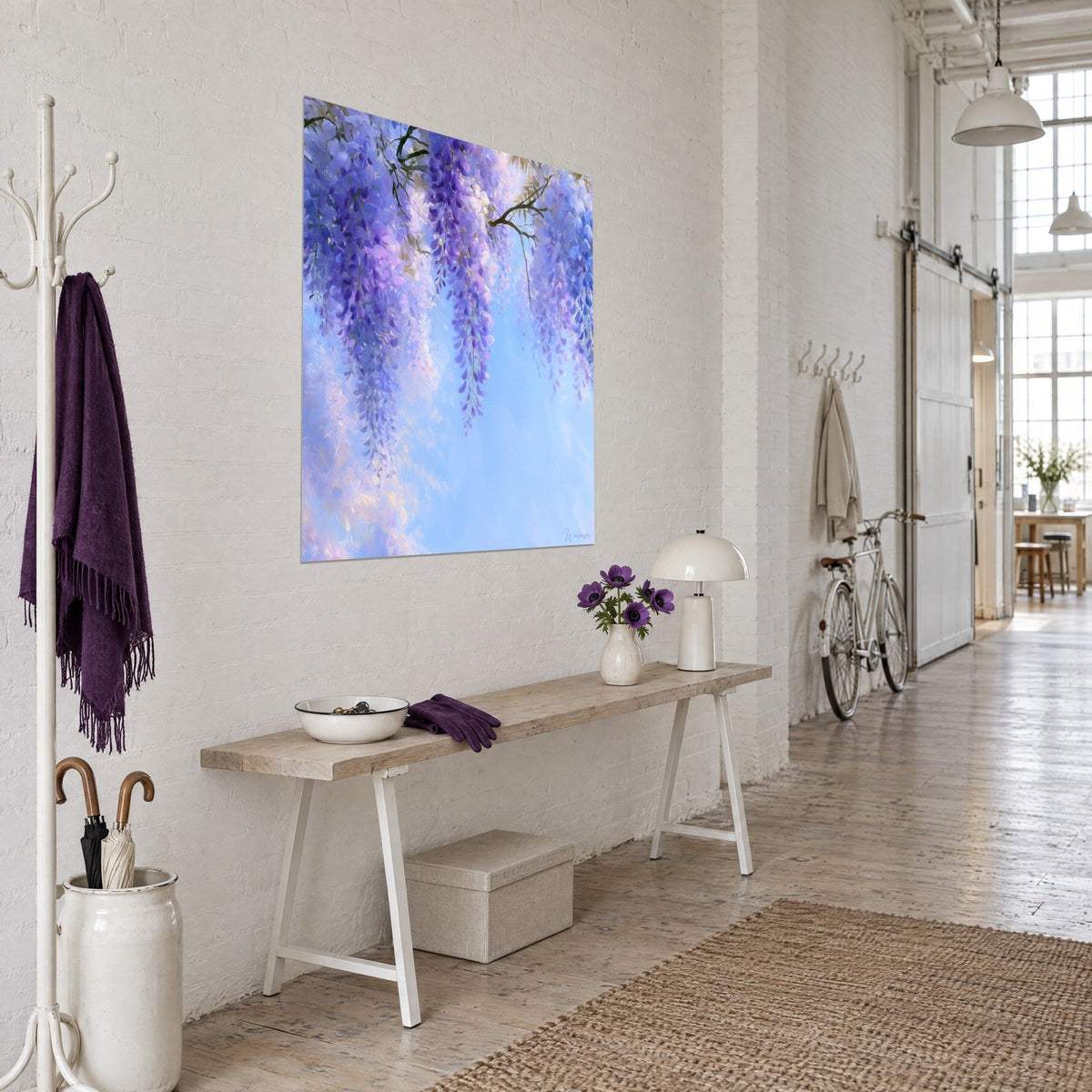 Quadro fiori di glicine pendenti, malva e blu periwinkle, ramo marrone, su parete bianca accanto a una consolle in legno