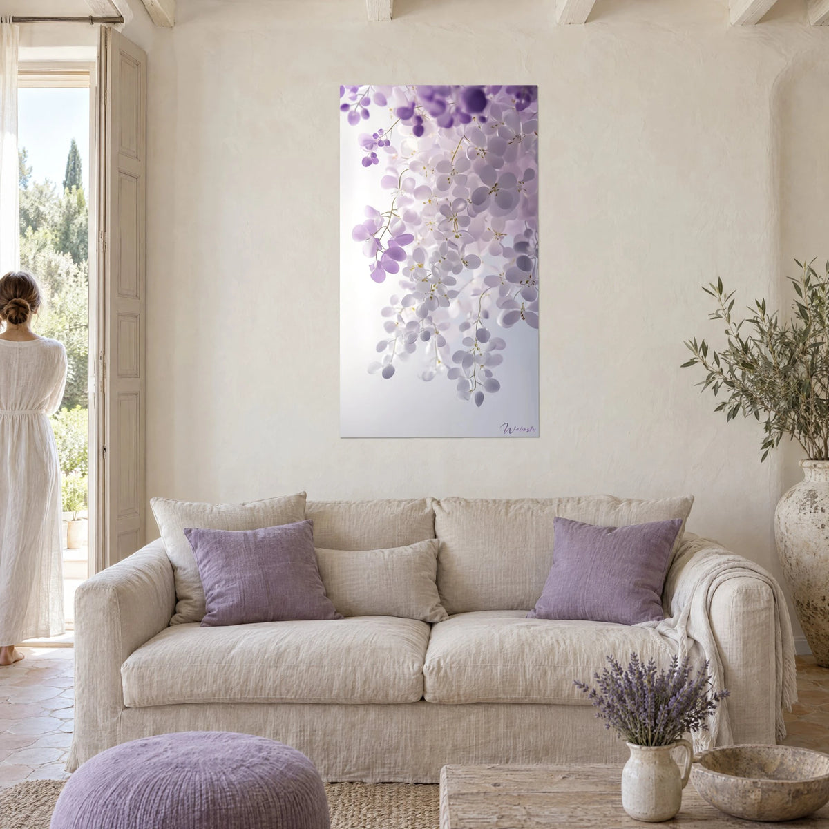 Tableau grappes de glycine lilas et blanches pendant sur fond nacré, au-dessus d'un canapé dans un salon lumineux