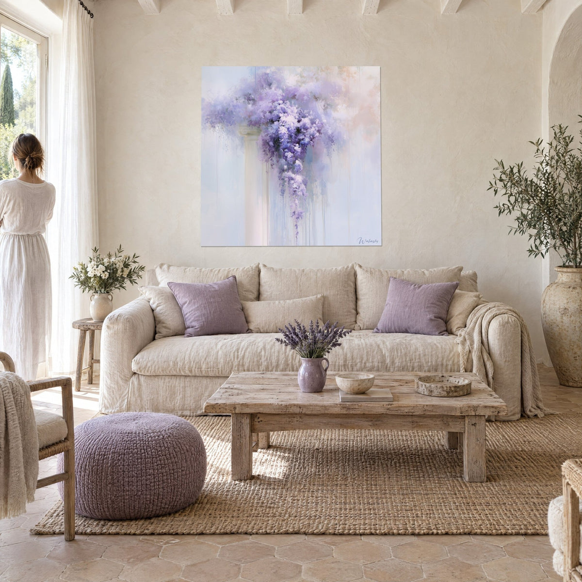 Wall art with mauve wisteria cascading down an ivory column, misty blue background; a woman seen from behind above a sofa in a bright living room