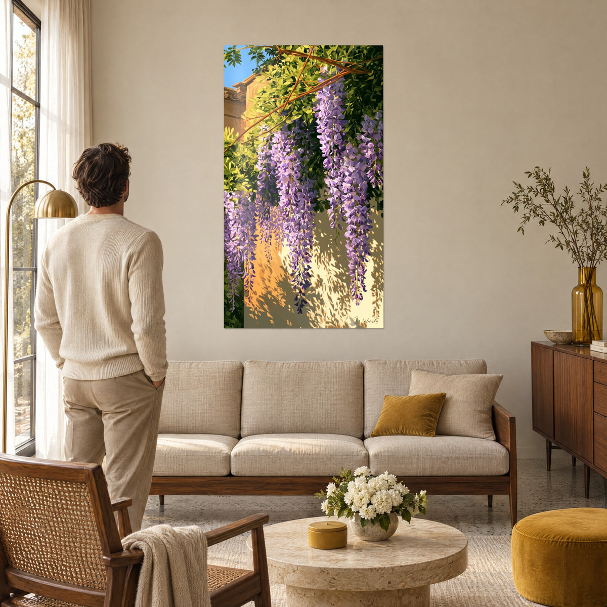 Schilderij blauweregen in paarse trossen op een okerkleurige gevel, zacht groen gebladerte, man van achteren, boven een bank in een lichte woonkamer