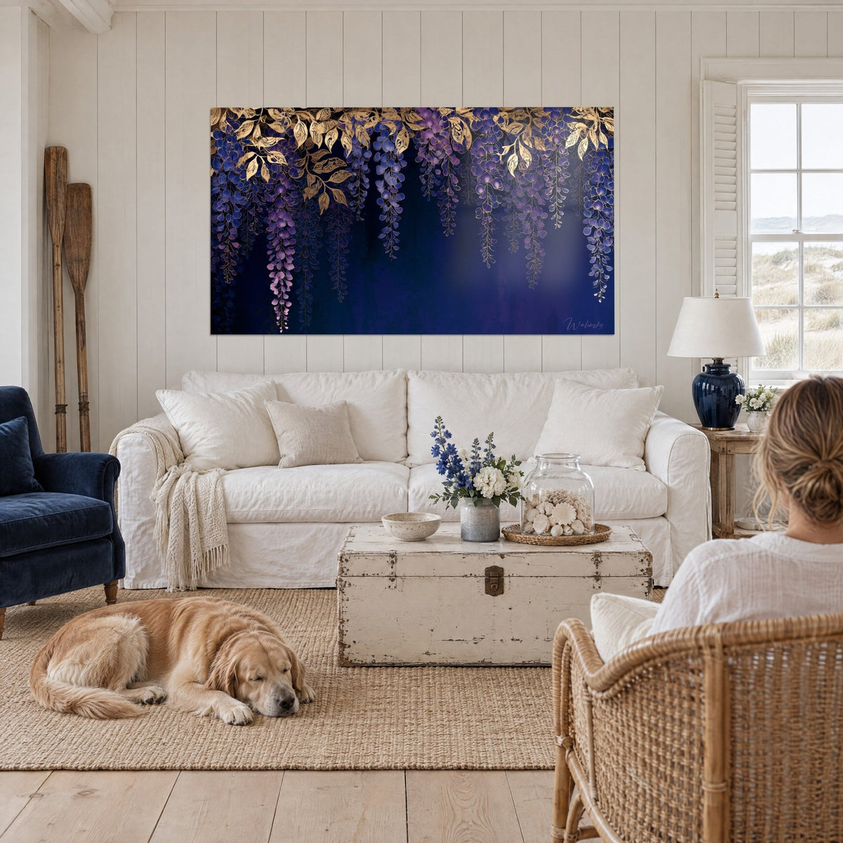 Quadro con glicine viola in grappoli pendenti e foglie dorate su fondo blu notte, sopra un divano in un soggiorno luminoso