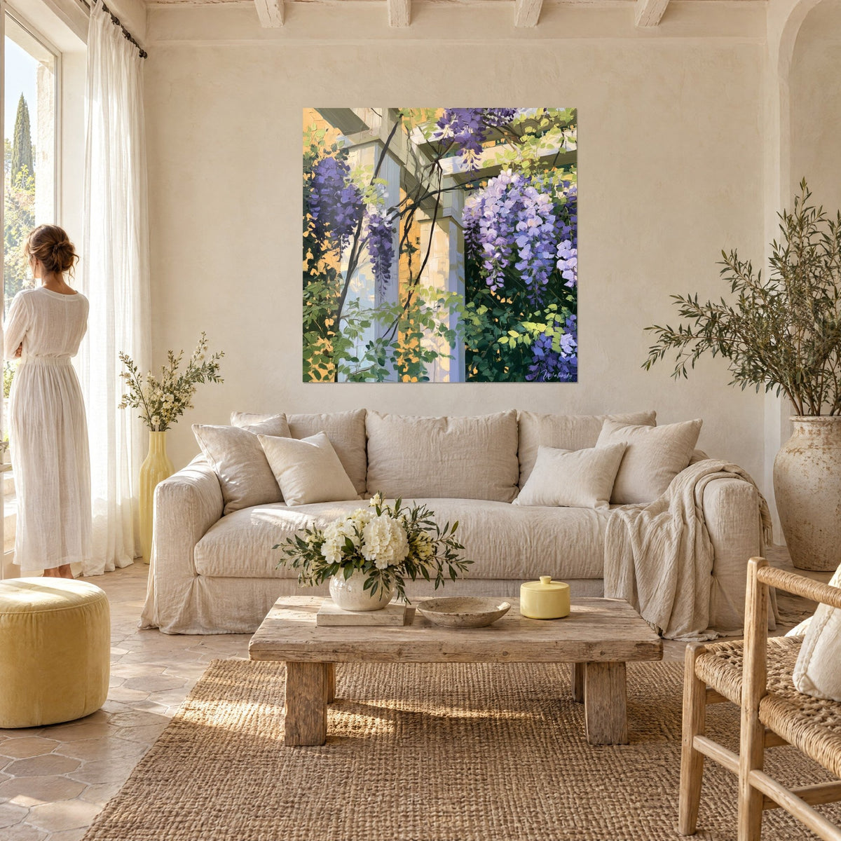 Quadro glicine in grappoli viola su colonne color crema, fogliame verde tenero, donna di spalle, sopra un divano in un soggiorno luminoso
