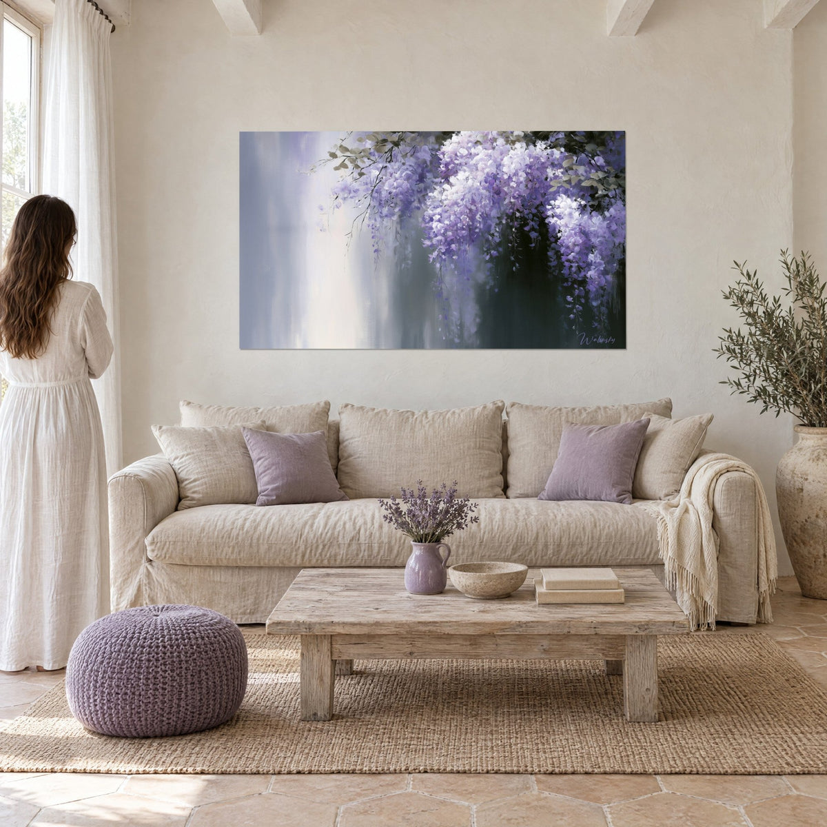 Wall art wisteria in violet and white clusters on silver-grey background, woman seen from behind, above a sofa in a bright living room