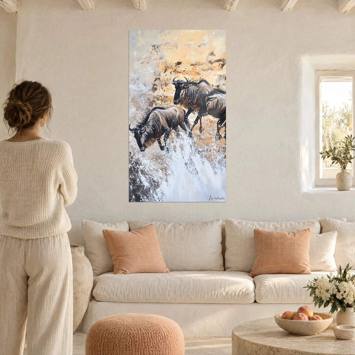 Tableau gnous bondissant dans l'écume blanche, robes brunes et fond ocre, femme de dos au-dessus d'un canapé dans un salon lumineux