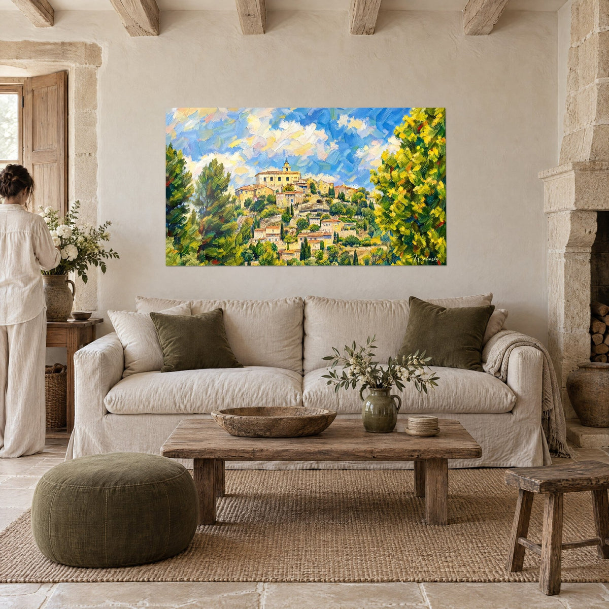 Cuadro pueblo encaramado de fachadas ocre bajo un cielo azul y crema, mimosa amarilla a la derecha, sobre un sofá en un salón luminoso