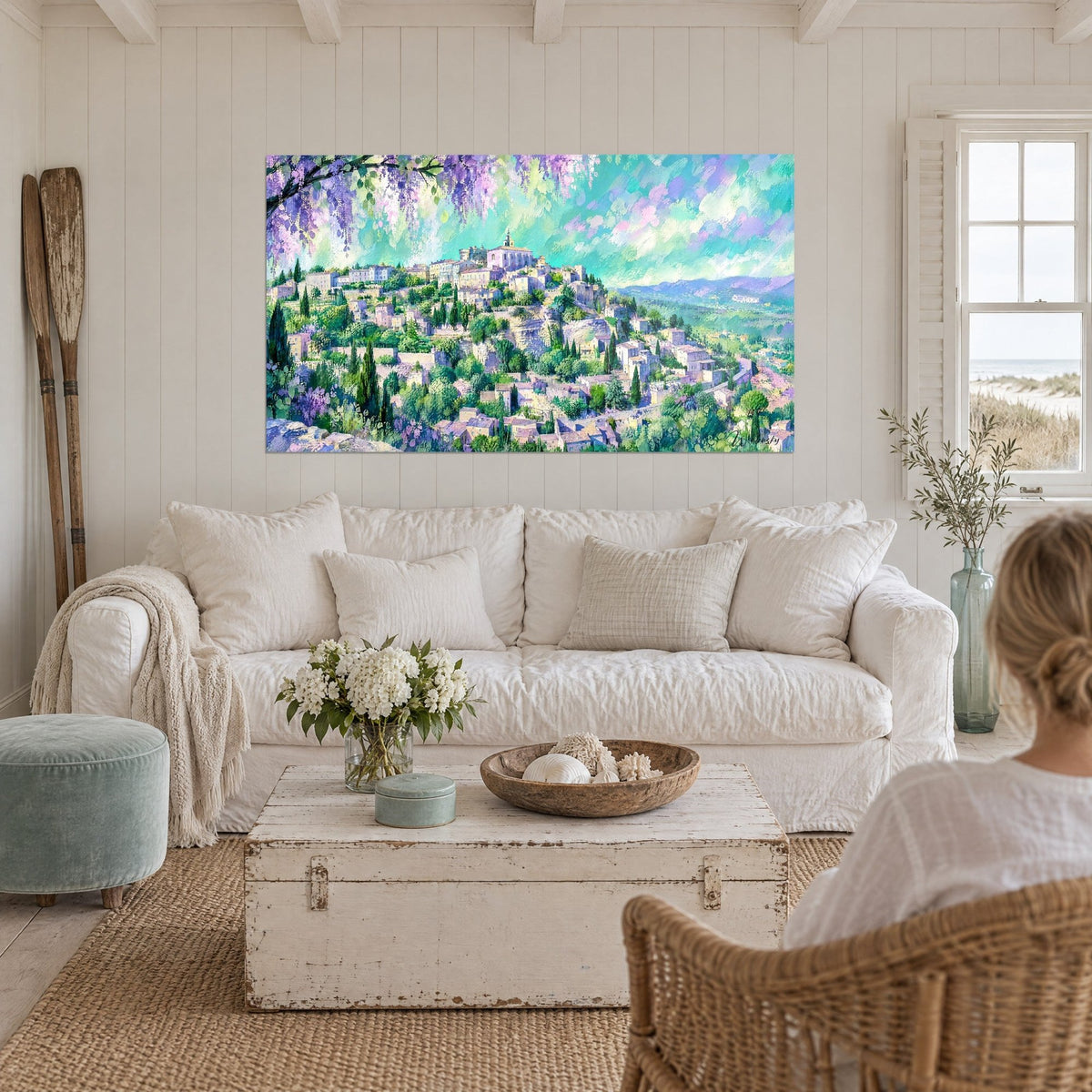 Wall art hilltop village with pink rooftops and dark cypress trees, purple wisteria above, turquoise sky, above a sofa in a bright living room