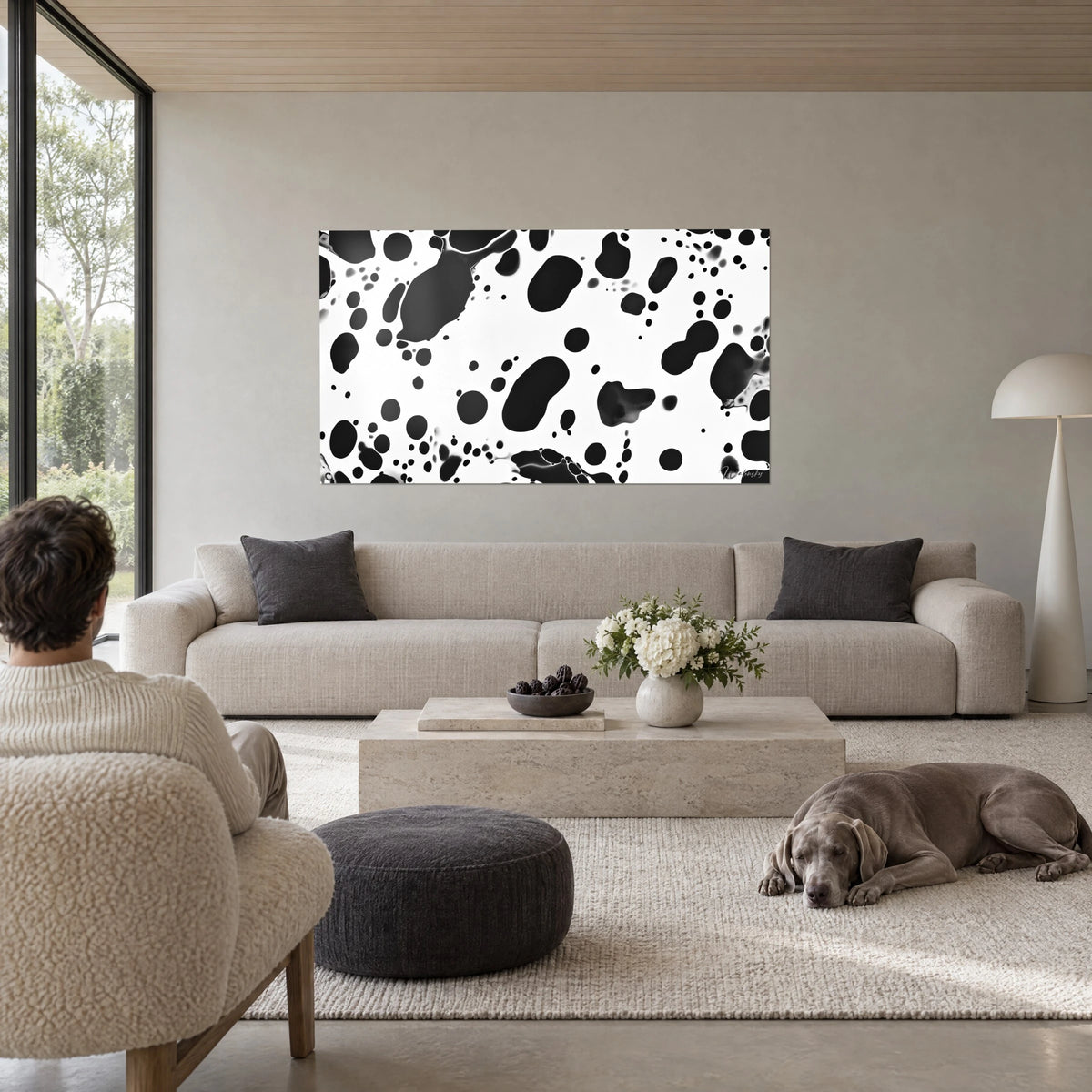 Cuadro con manchas negras de vaca sobre fondo blanco, charcos ovalados de tinta, hombre de espaldas y galgo gris, encima de un sofá en un salón luminoso