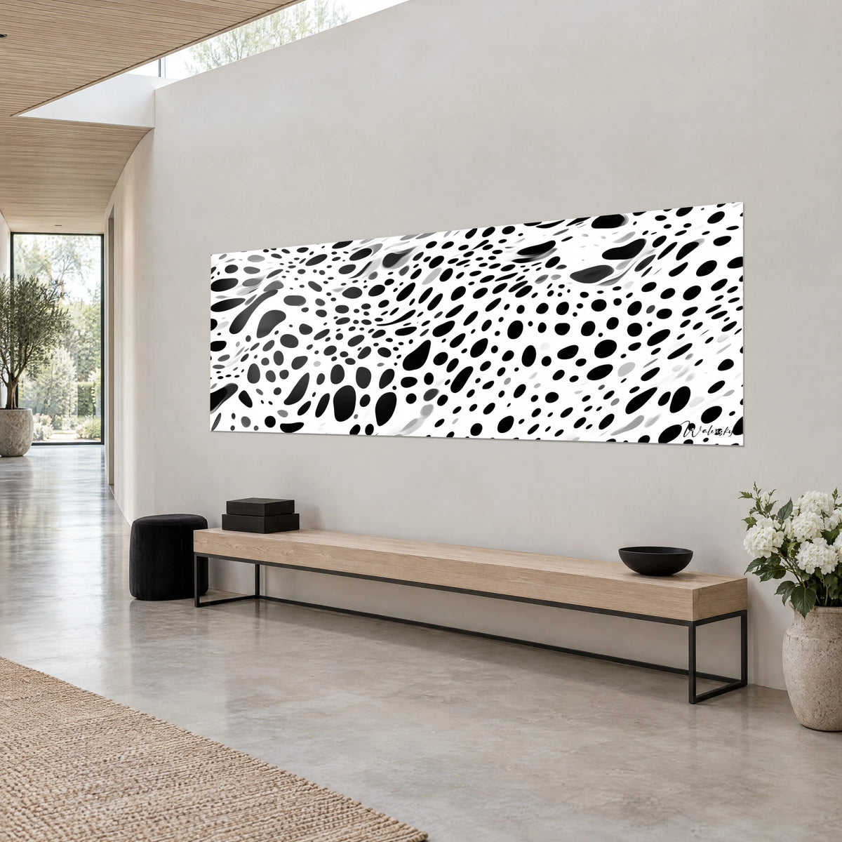 Quadro motivo leopardato astratto, gocce nere e grigie su bianco puro, appeso a una parete grigia accanto a una panca in legno