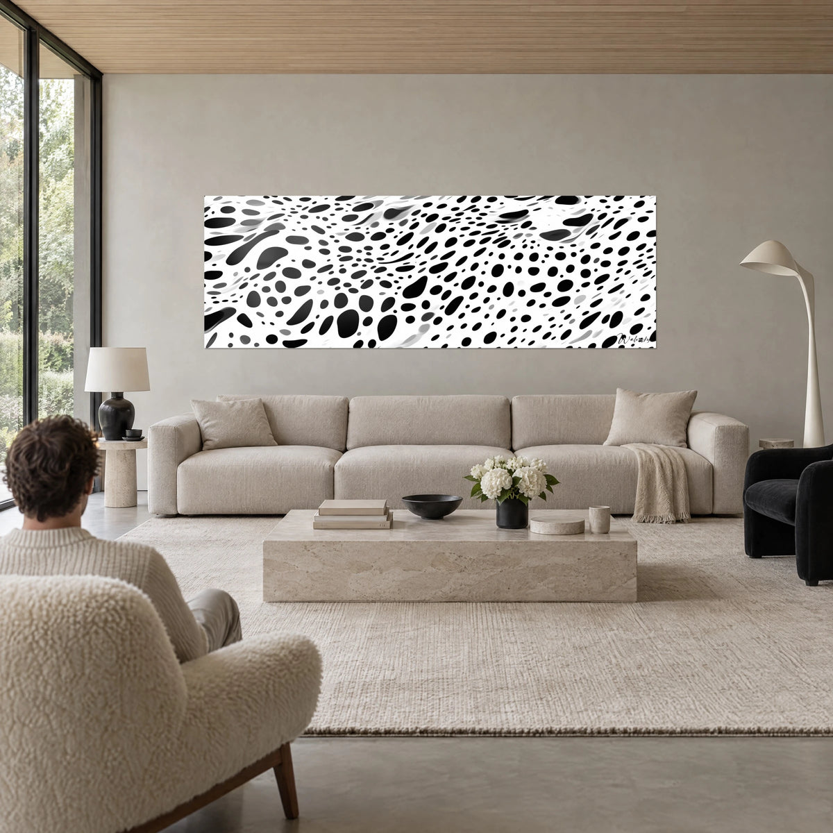 Quadro panoramico maculato, macchie nere ovali su fondo bianco, persona di spalle, sopra un divano in un soggiorno luminoso