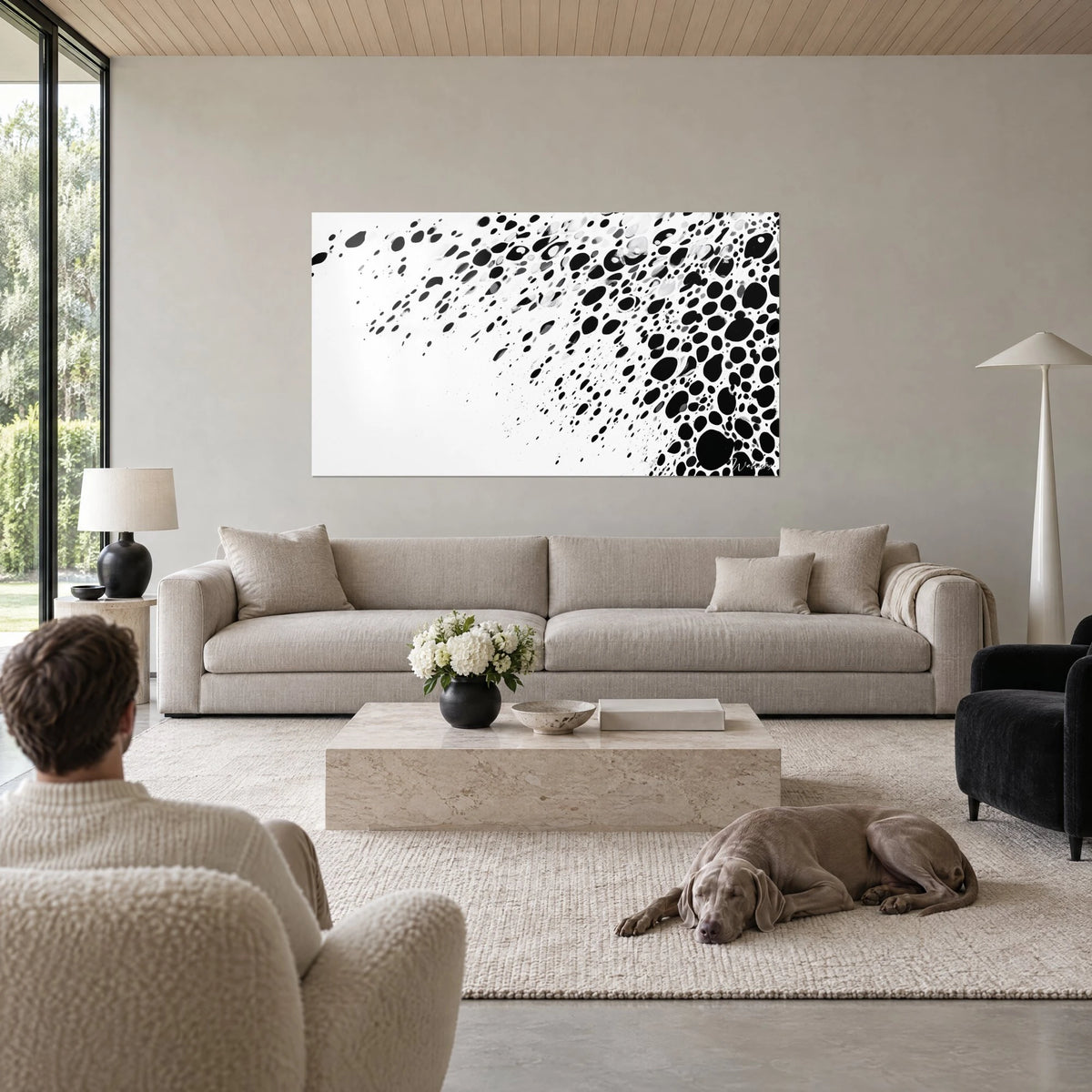 Cuadro de gotas de tinta negra salpicando un fondo blanco, dos personas de espaldas, Weimaraner gris, encima de un sofá en un salón luminoso