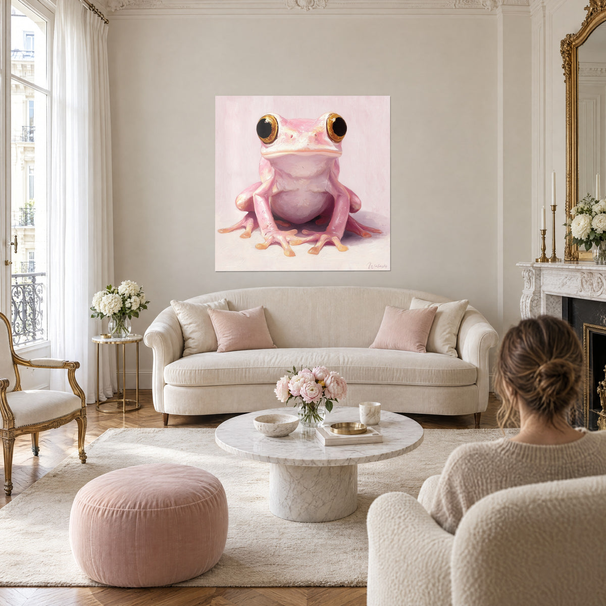 Wall art of a pink frog with large golden eyes on a powdery background, viewed from behind by a woman, above a sofa in a bright living room