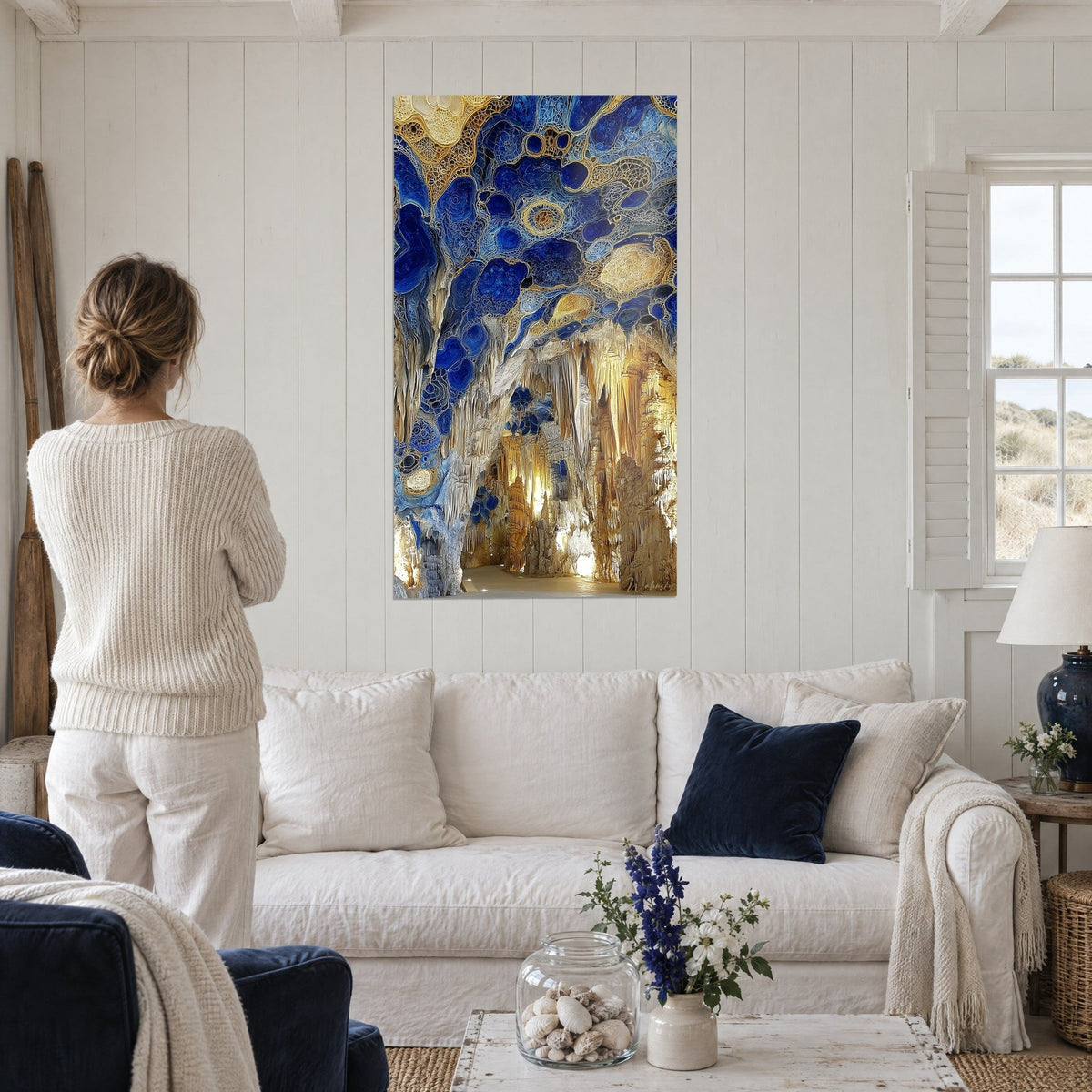 Gemälde Grotte mit goldenen Stalaktiten unter einem kobaltblauen Gewölbe, von hinten gesehen von einer Frau über einem Sofa in einem hellen Wohnzimmer