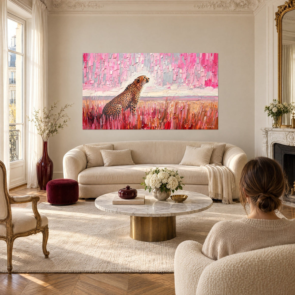 Wall art of a spotted wild cat sitting in tawny and pink grass, pink and grey sky, above a sofa in a bright living room