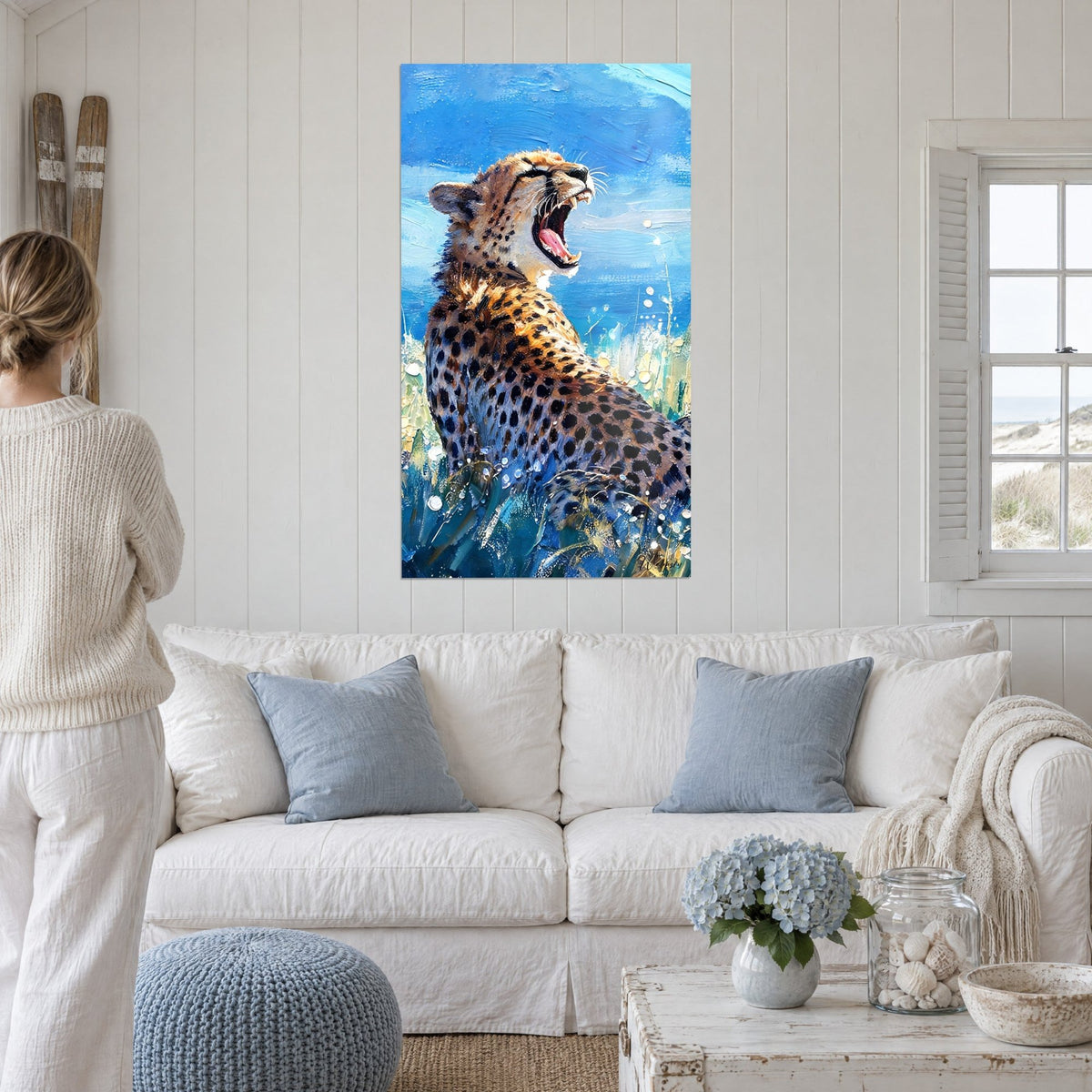 Schilderij brullende jachtluipaard tegen een blauwe lucht, okerkleurige vacht met zwarte vlekken, gouden gras, boven een bank in een lichte woonkamer