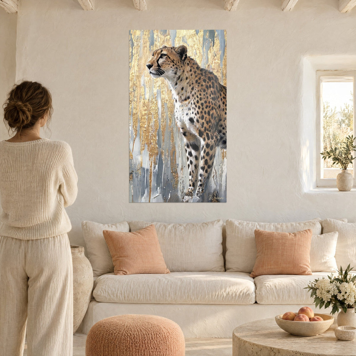 Wall art of a spotted wild cat with tawny fur, background of gold and silver drips, woman seen from behind, above a sofa in a bright living room