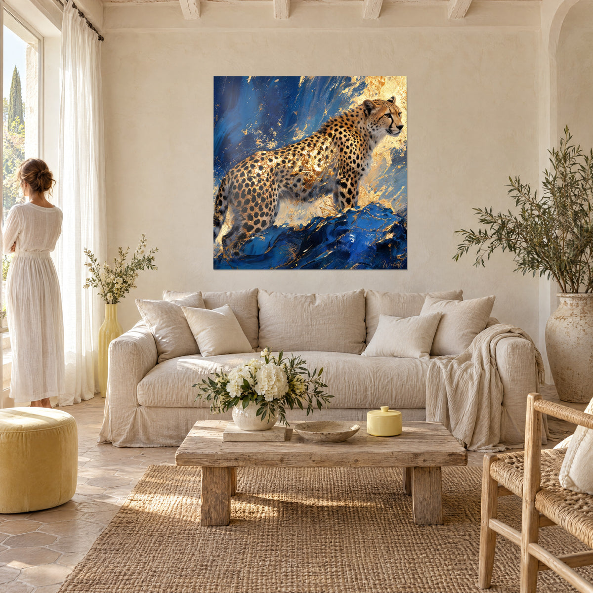 Tableau guépard tacheté aux flancs dorés sur roche bleu marine, femme en robe blanche de dos, au-dessus d'un canapé dans un salon lumineux