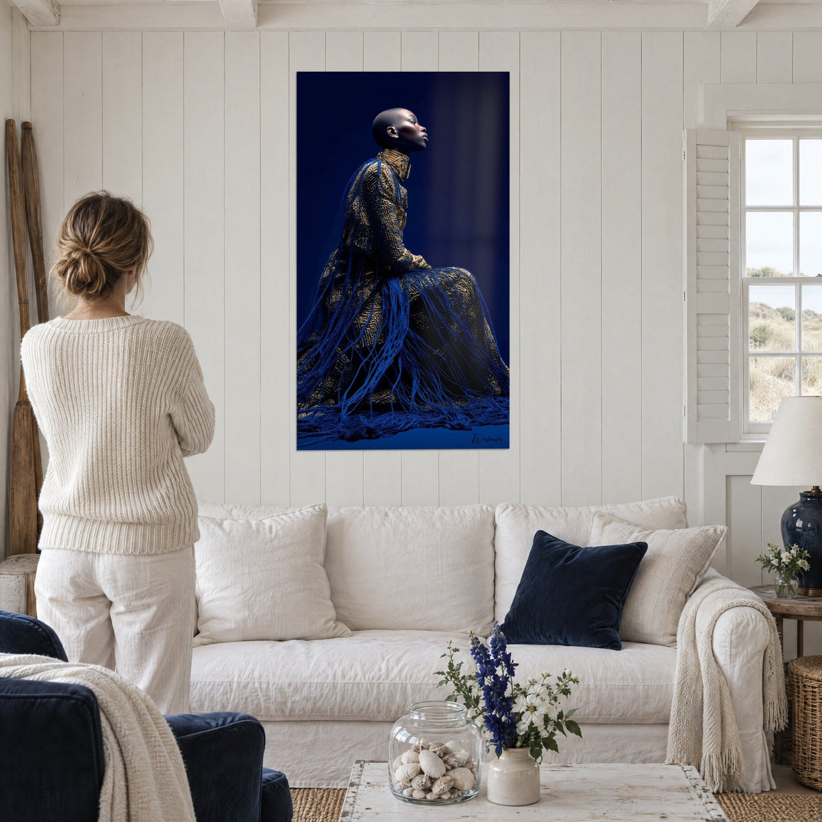 Tableau femme au crâne rasé en profil, robe dorée et fils bleu cobalt, salon blanc, au-dessus d'un canapé dans un salon lumineux