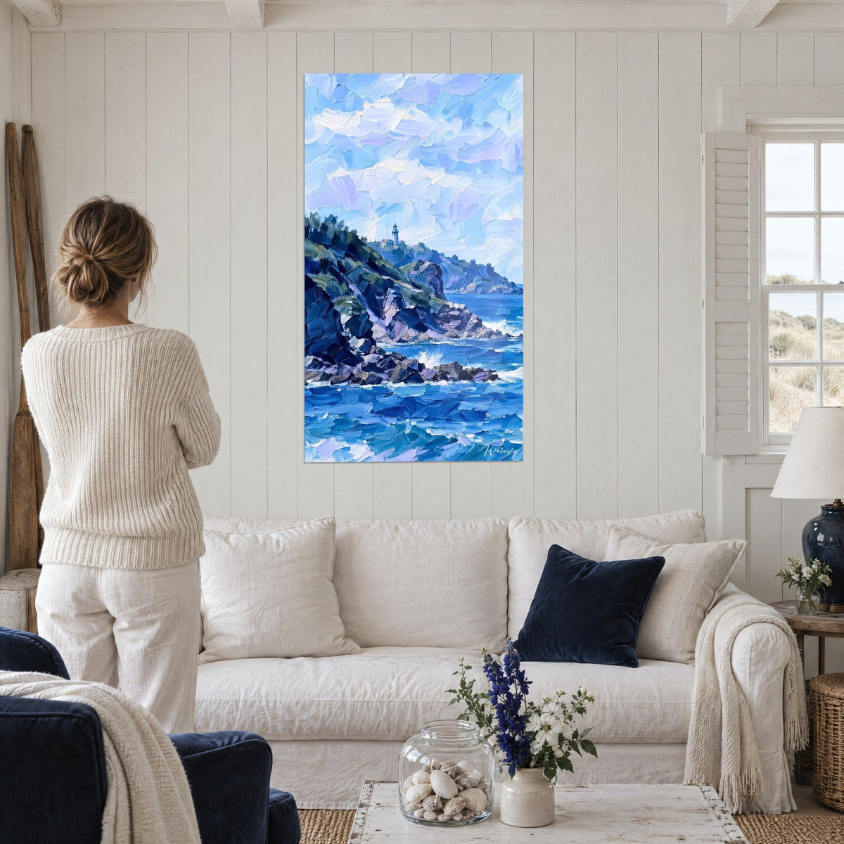 Gemälde Leuchtturm weiß auf Klippe, lavendelblauer Himmel und indigoblaue Wellen, über einem Sofa in einem hellen Wohnzimmer