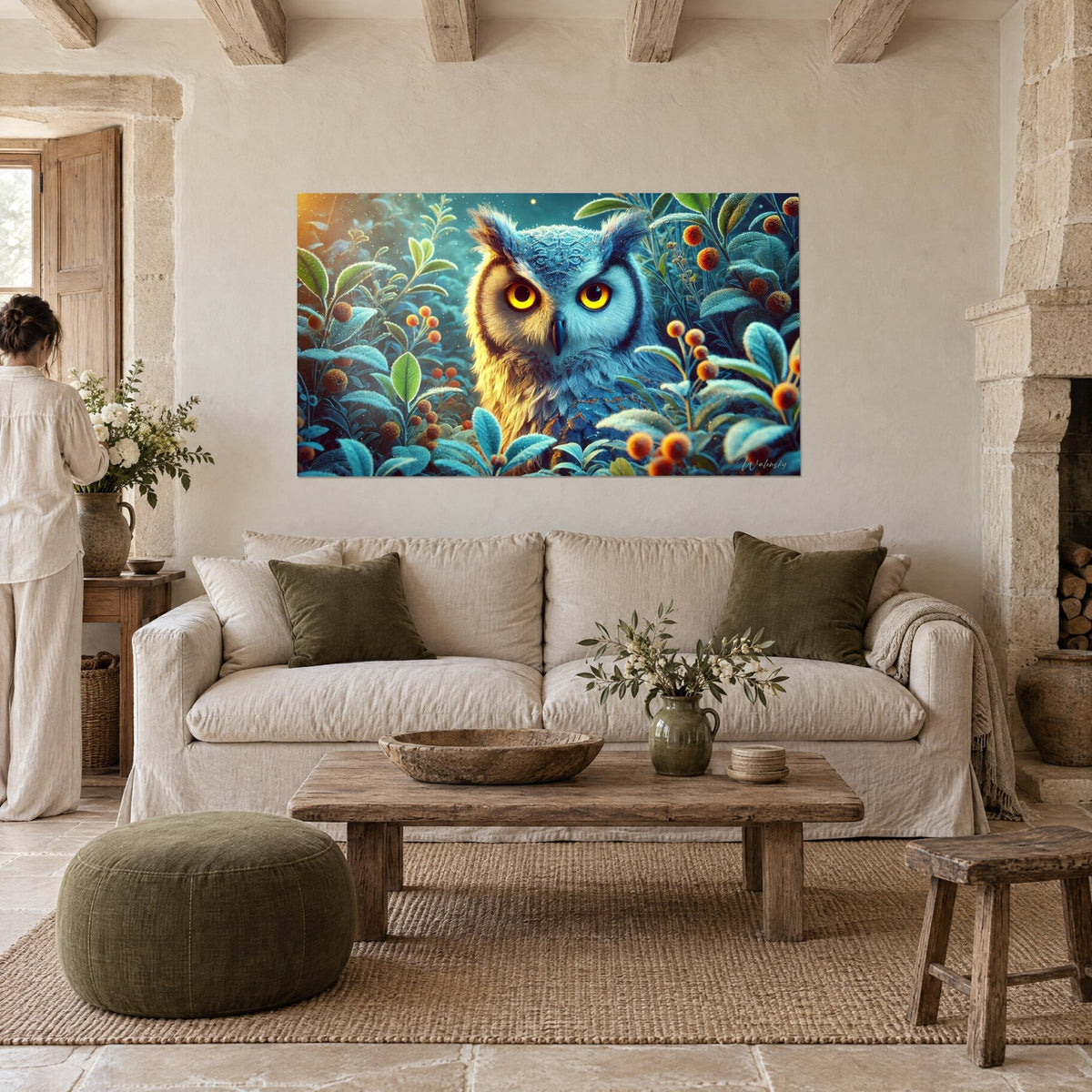 Wall art of an owl with bright yellow eyes, frosted blue plumage and orange berries, a woman seen from behind, above a sofa in a bright living room