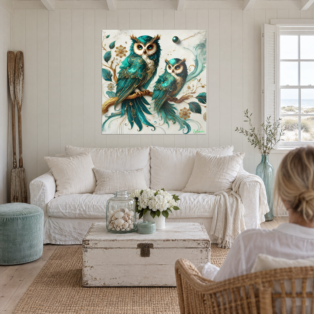 Tableau couple de hiboux émeraude à plumes filigranées d'or, perchés sur une branche, au-dessus d'un canapé dans un salon lumineux