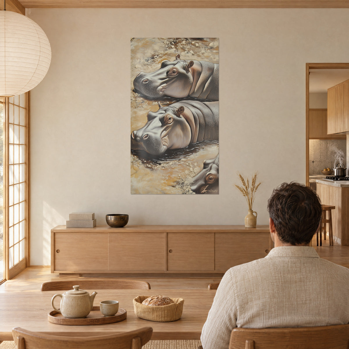 Cuadro de hipopótamos somnolientos pintados en gris ceniza y arena, baño de barro, hombre de espaldas en la mesa, comedor japandi en madera clara