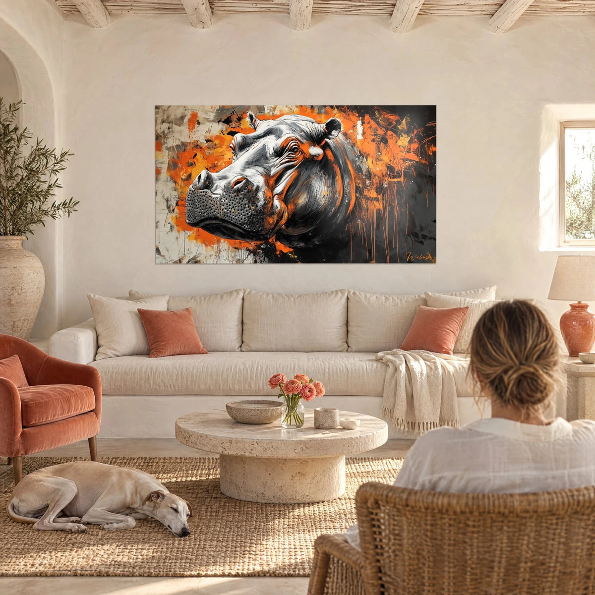 Wall art silvery grey hippo splashed with bright orange, viewed by a woman from behind, above a sofa in a bright living room