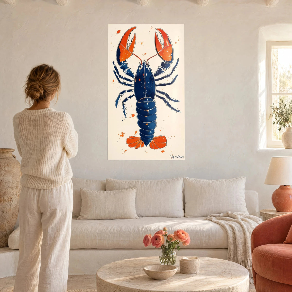 Tableau homard bleu marine aux pinces orange, fond crème, devant une femme de dos, au-dessus d'un canapé dans un salon lumineux