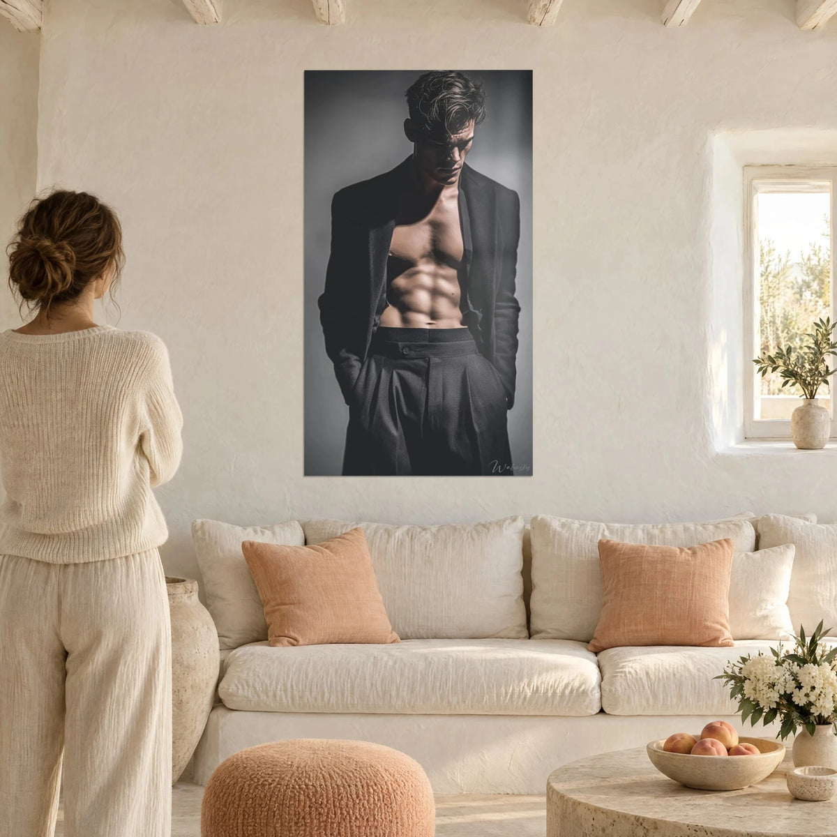 Quadro giovane uomo a torso nudo sotto una giacca antracite, ciocche castane, sfondo grigio, sopra un divano in un soggiorno luminoso