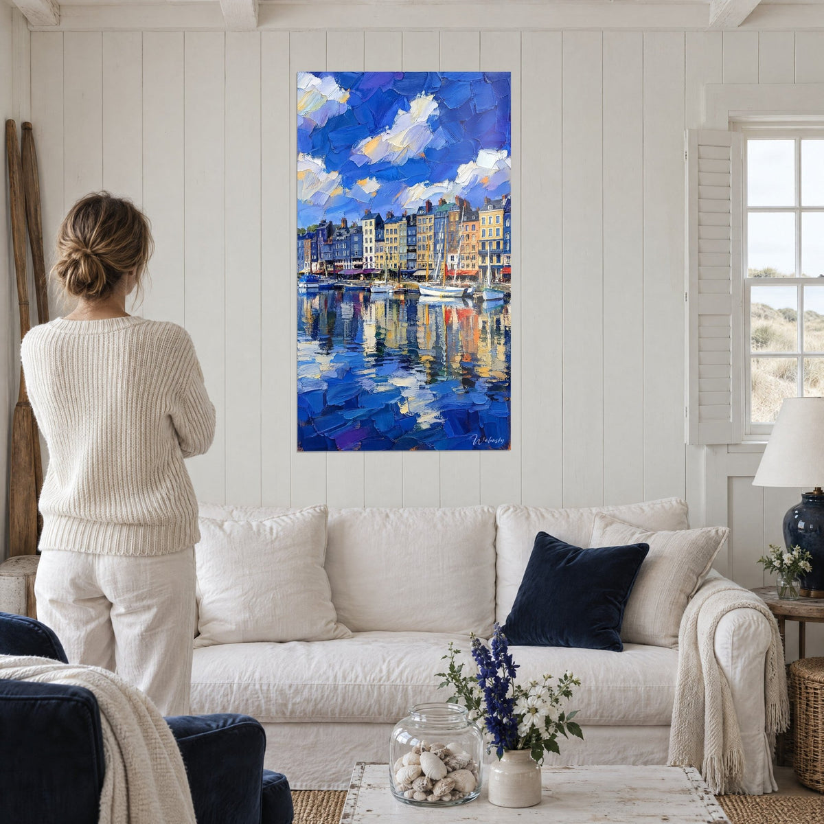 Quadro vecchio porto di Honfleur con facciate ocra e blu, cielo di nuvole bianche, sopra un divano in un soggiorno luminoso