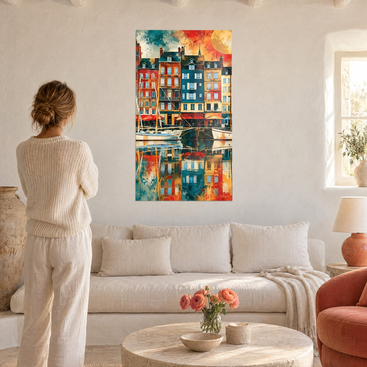 Cuadro fachadas del puerto de Honfleur en azul petróleo y rojo ladrillo, reflejos en el agua, mujer de espaldas sobre un sofá en un salón luminoso