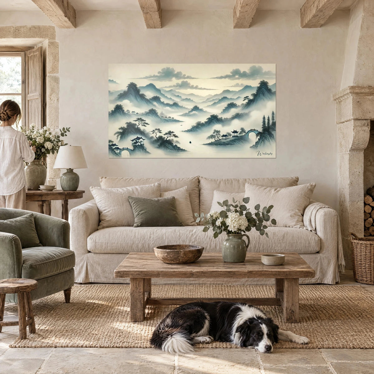Wall art of mountains drowned in blue-green mist on a cream background, pavilion and small bridge, a recumbent collie, above a sofa in a bright living room