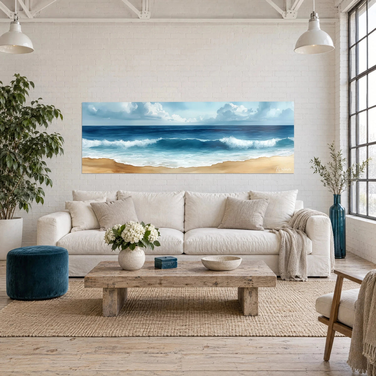 Wall art of frothy turquoise surf on ochre sand, pale blue cloudy sky, above a sofa in a bright living room