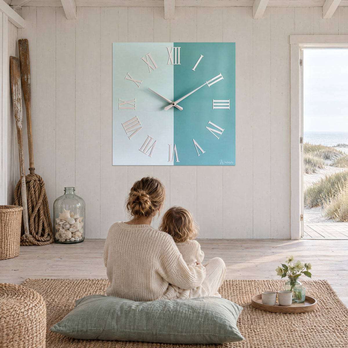 Tableau grande horloge carrée turquoise et vert d'eau, chiffres romains blancs, mère et enfant de dos assis sur un coussin sauge, salon face à la mer