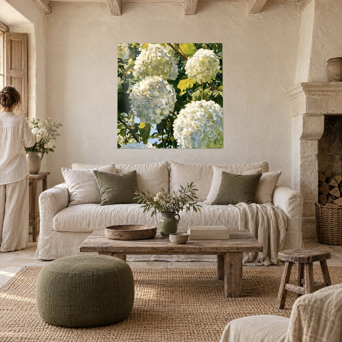 Wall art with large balls of white and ivory hydrangeas, soft green leaves and blue sky, above a sofa in a bright living room