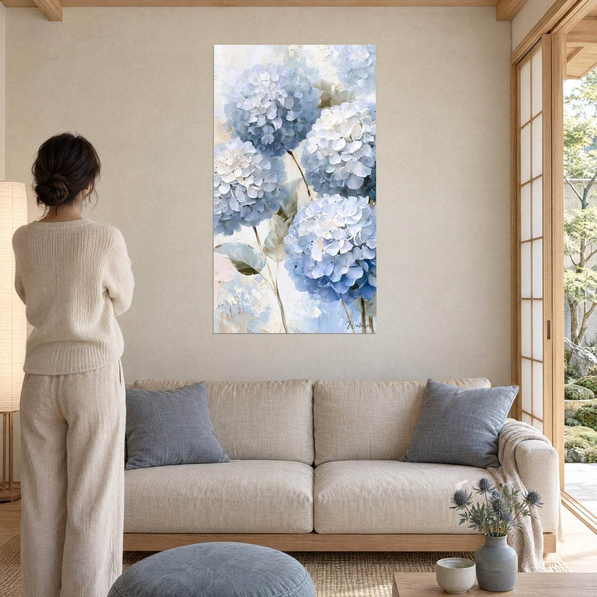 Wall art sky blue hydrangeas with thick white petals, beige stems, woman seen from behind, above a sofa in a bright living room