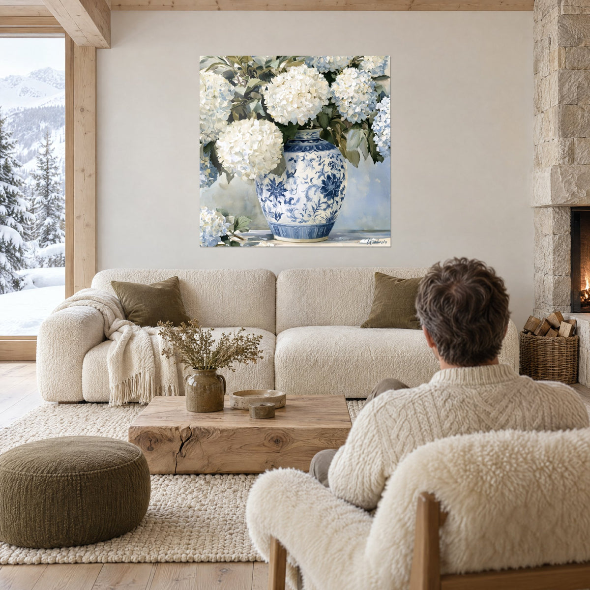 Wall art white hydrangeas in large creamy blooms, blue and white vase with a floral pattern, above a sofa in a bright living room