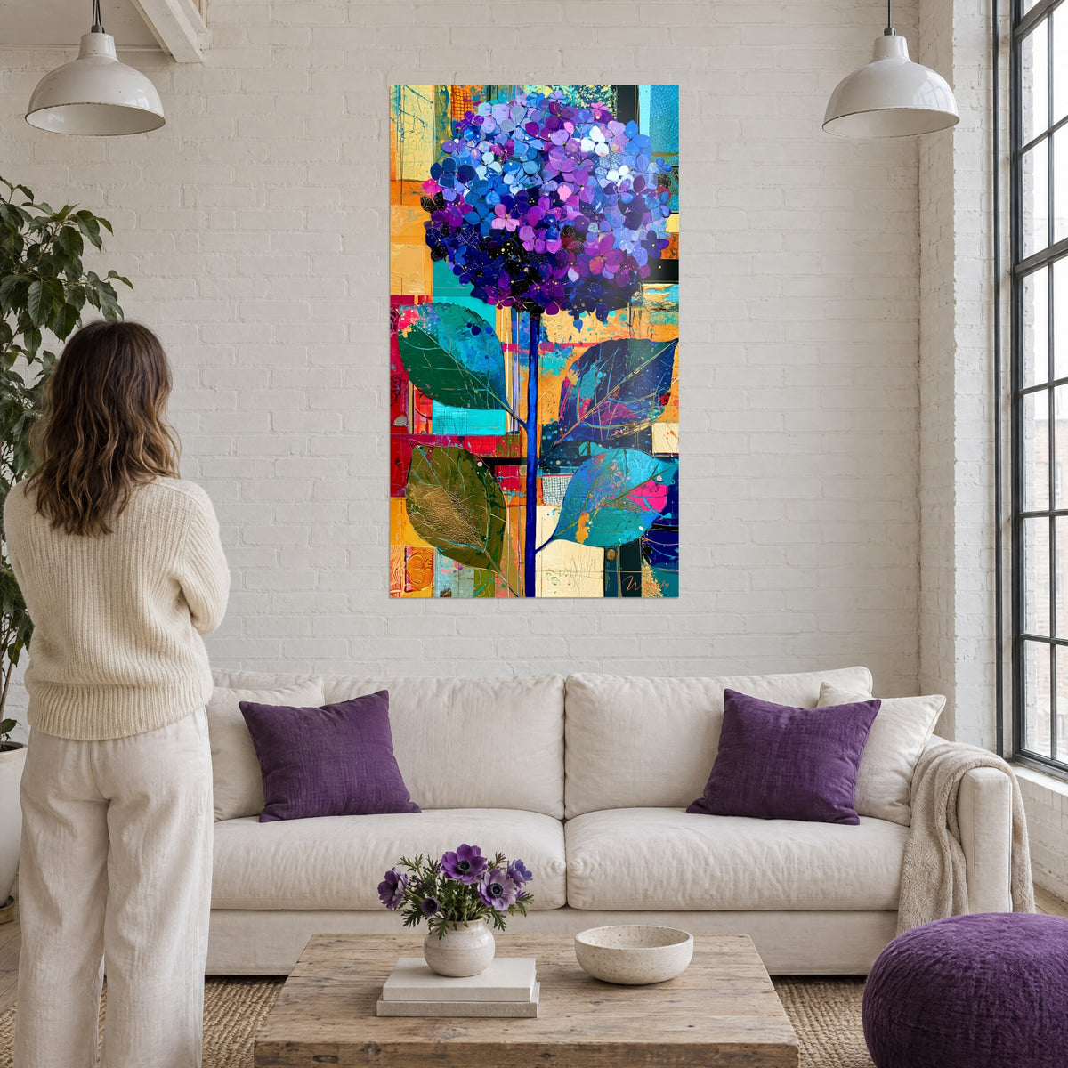 Schilderij hortensia bloesem in paars en blauw op okerkleurige patchwork achtergrond, vrouw van achteren, boven een bank in een lichte woonkamer