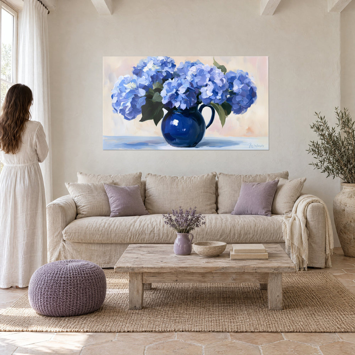 Wall art lavender-blue hydrangea bouquet in a navy blue pitcher, blush beige background, above a sofa in a bright living room