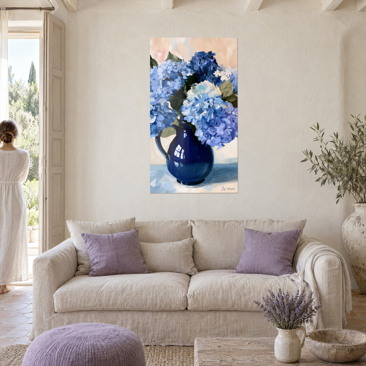Wall art of blue hydrangeas in a navy ceramic pitcher, peach background, above a sofa in a bright living room