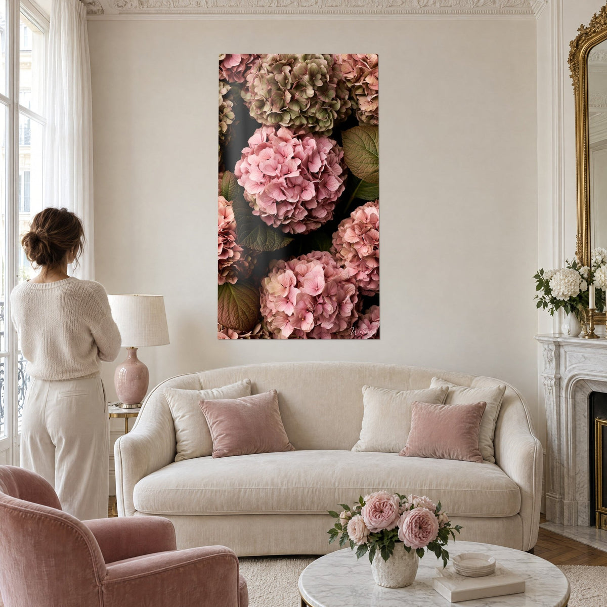 Wall art bouquet of powder-pink hydrangeas on dark green foliage, seen from behind a woman, above a sofa in a bright living room