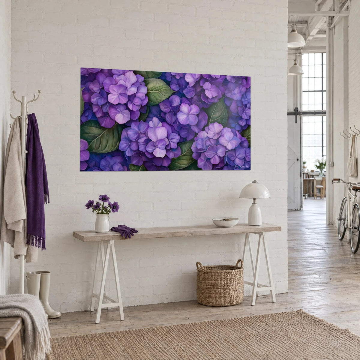 Cuadro de corolas apretadas de hortensia lila y violeta con hojas verdes, colgado en pared blanca junto a una consola de madera